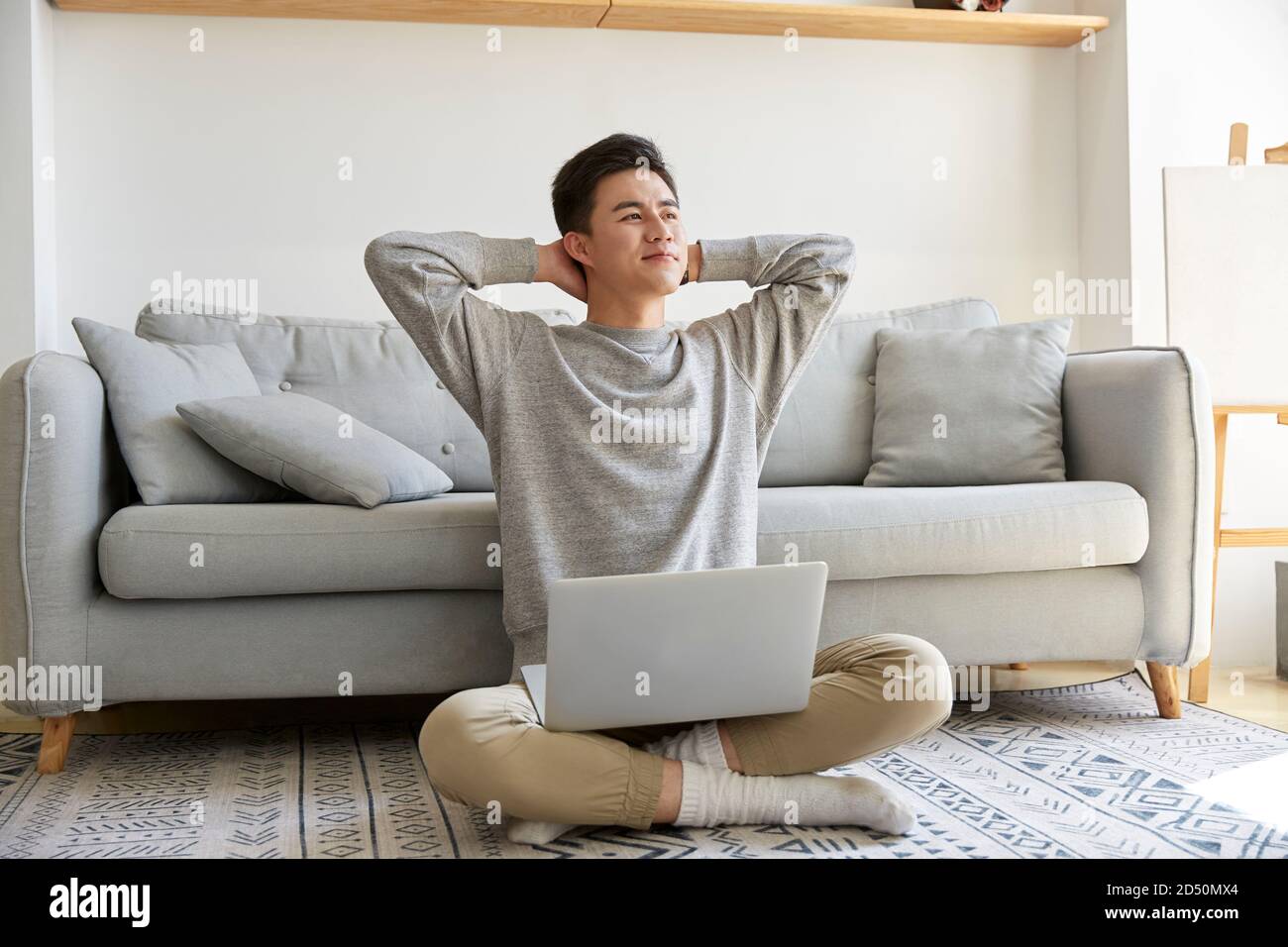 happy young asian business man staying at home sitting on carpet working using laptop computer happy and smiling Stock Photo