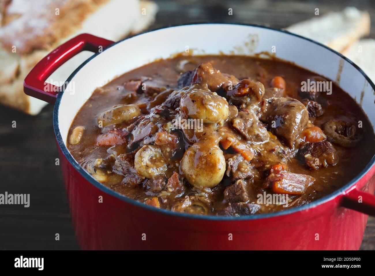 Beef Bourguignon cooked in an enameled cast iron Dutch oven and served with homemade artisan bread over a rustic wood background. Stock Photo