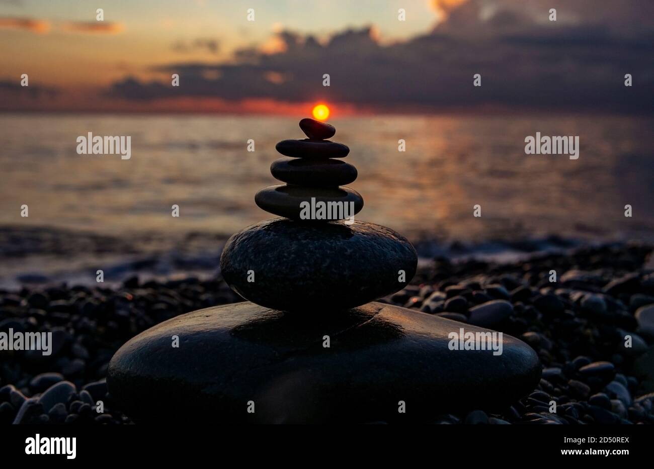 Stacked pebble stones on the background of a bright cloudy sky at sunset and the sea. Zen pebble pyramid, background, harmony and balance concept Stock Photo