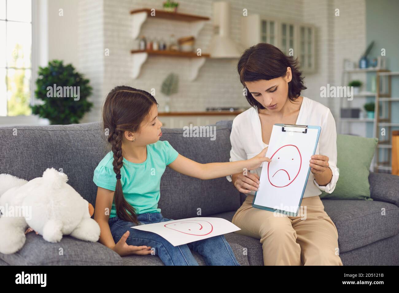 Pretty female child psychologist shows a little girl pictures with different emotions. Stock Photo