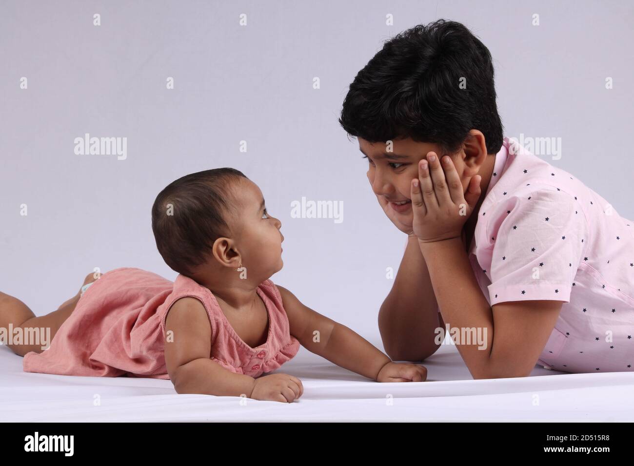 Cute little boy is playing with his younger sister at home lying on white backgroung. Stock Photo