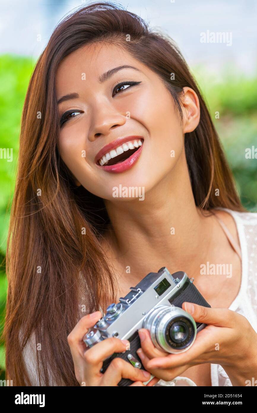 Beautiful Asian Chinese girl or young woman photographer outside laughing with perfect teeth taking pictures or photographs with a retro style camera Stock Photo