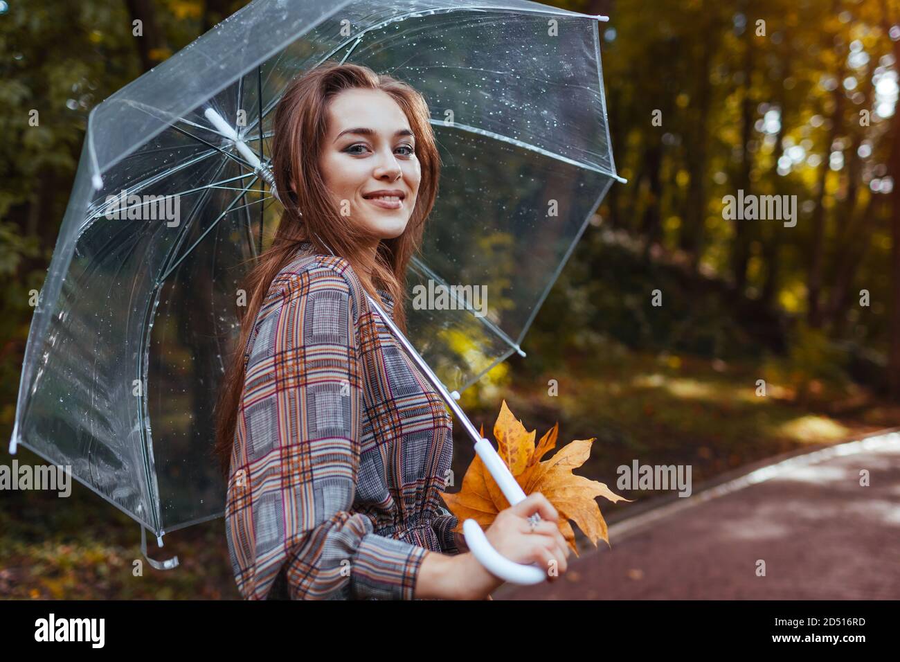 Portrait of young woman walking in park with transparent umbrella ...