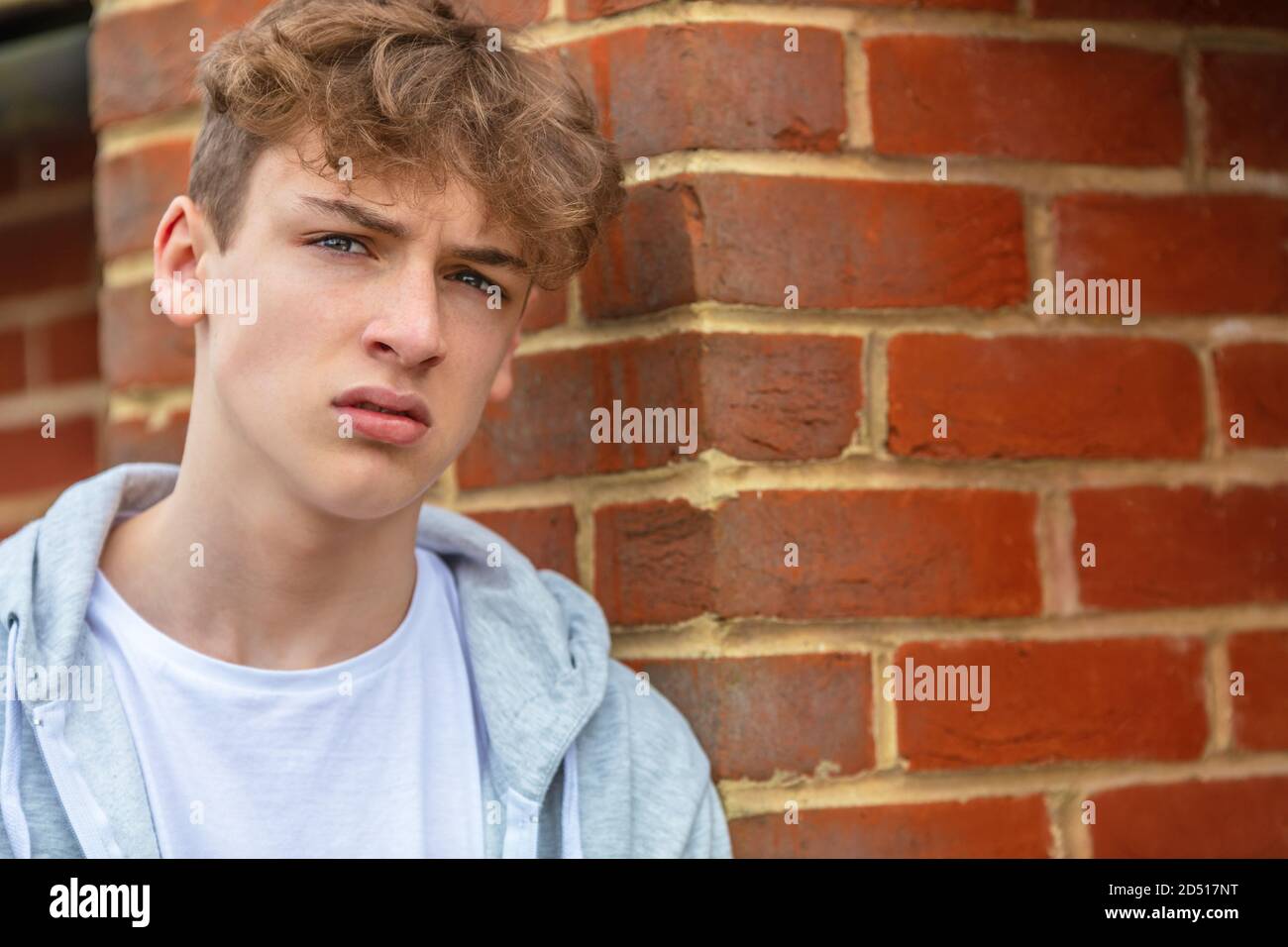 Serious male boy teenager outside leaning on brick wall wearing a gray hoody in urban city Stock Photo