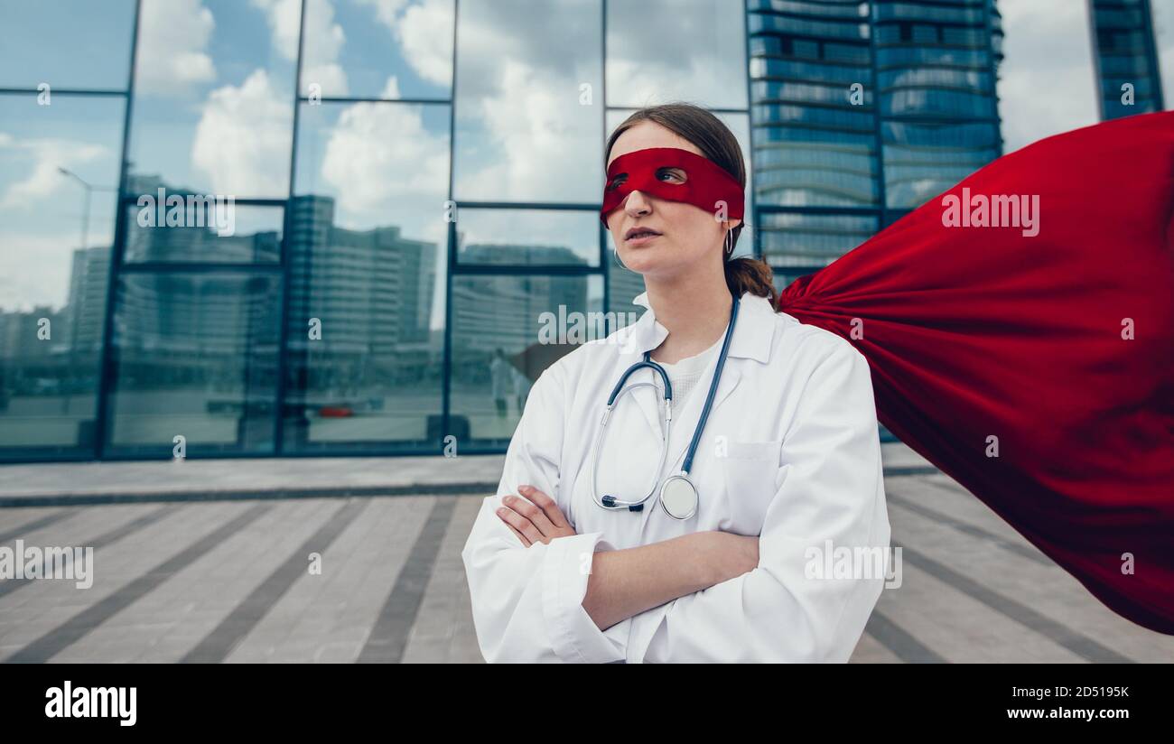 female paramedic in a superhero raincoat standing on a city street. Stock Photo