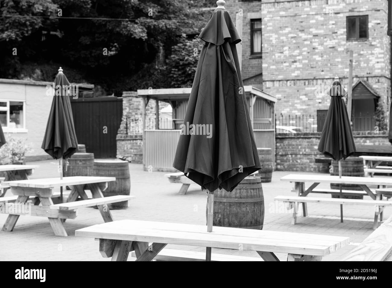 black and white image of close up of empty wooden tables and chairs with closed purple umbrellas outside restaurant with social distancing measures Stock Photo