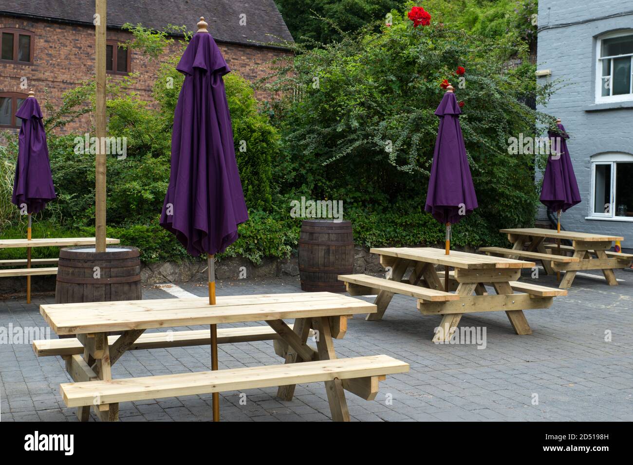 close up of empty wooden tables and chairs with closed purple umbrellas outside restaurant with social distancing measures in autumn Stock Photo