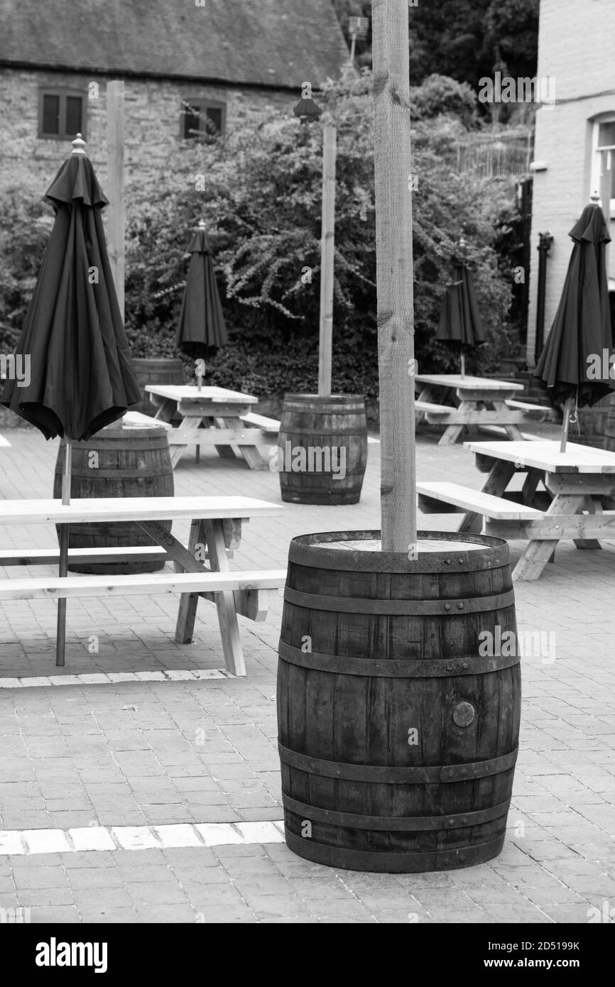 black and white image of close up of empty wooden tables and chairs with closed purple umbrellas outside restaurant with social distancing measures Stock Photo