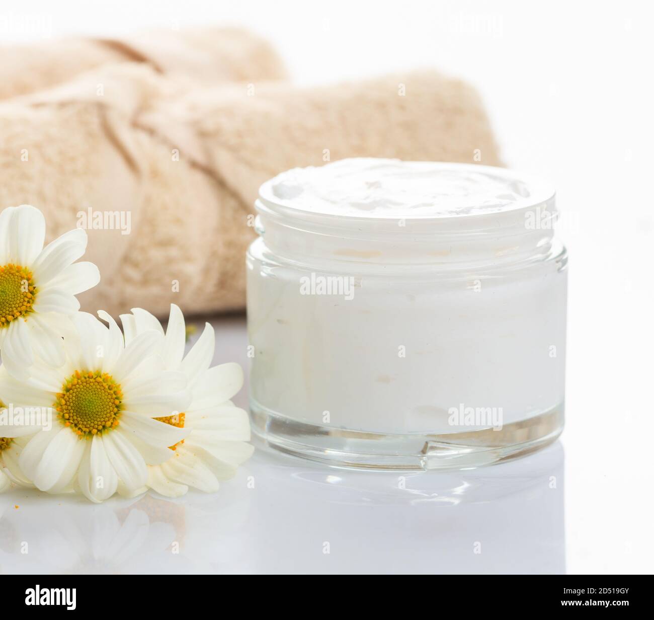 Moisturizing cream in glass jar and chamomile on white background. Camomile cosmetics for face and body with herbal protection. Close up view. Stock Photo