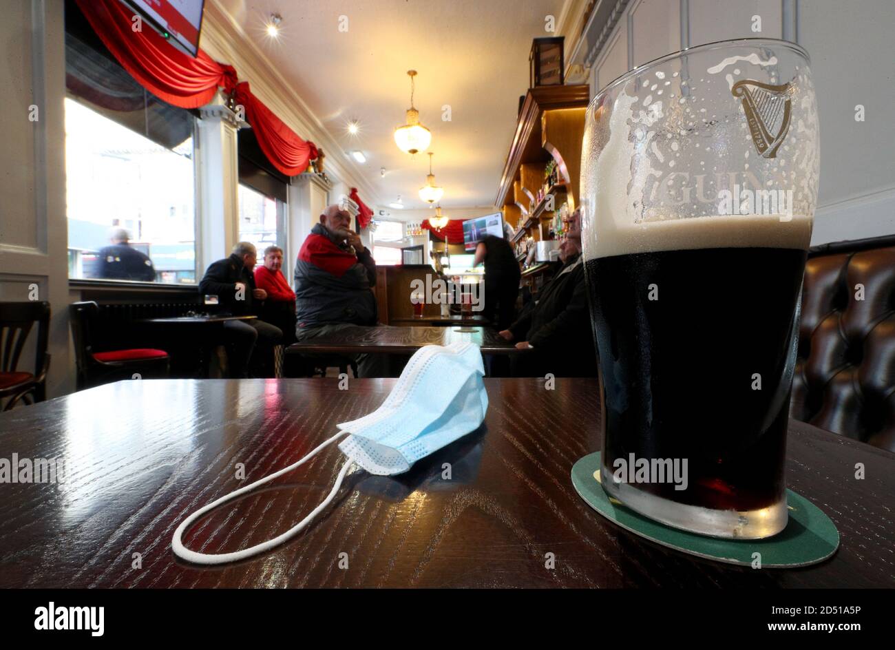 A close up of a pint of Guinness and a face mask on a table in the Richmond pub in Liverpool watch a statement by the Prime Minister Boris Johnson, as parts of the North of England are bracing themselves for the most stringent Tier 3 controls, with Merseyside expected to have its pubs, gyms and casinos closed in a bid to suppress its infection rate. Stock Photo