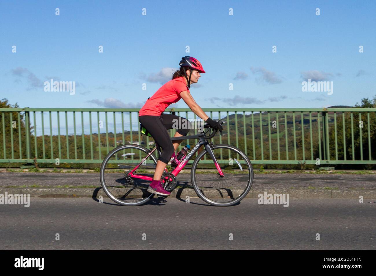 A female cyclist riding a Boardman carbon fibre sports road bike bicycle on countryside route crossing motorway bridge in rural Lancashire, UK Stock Photo