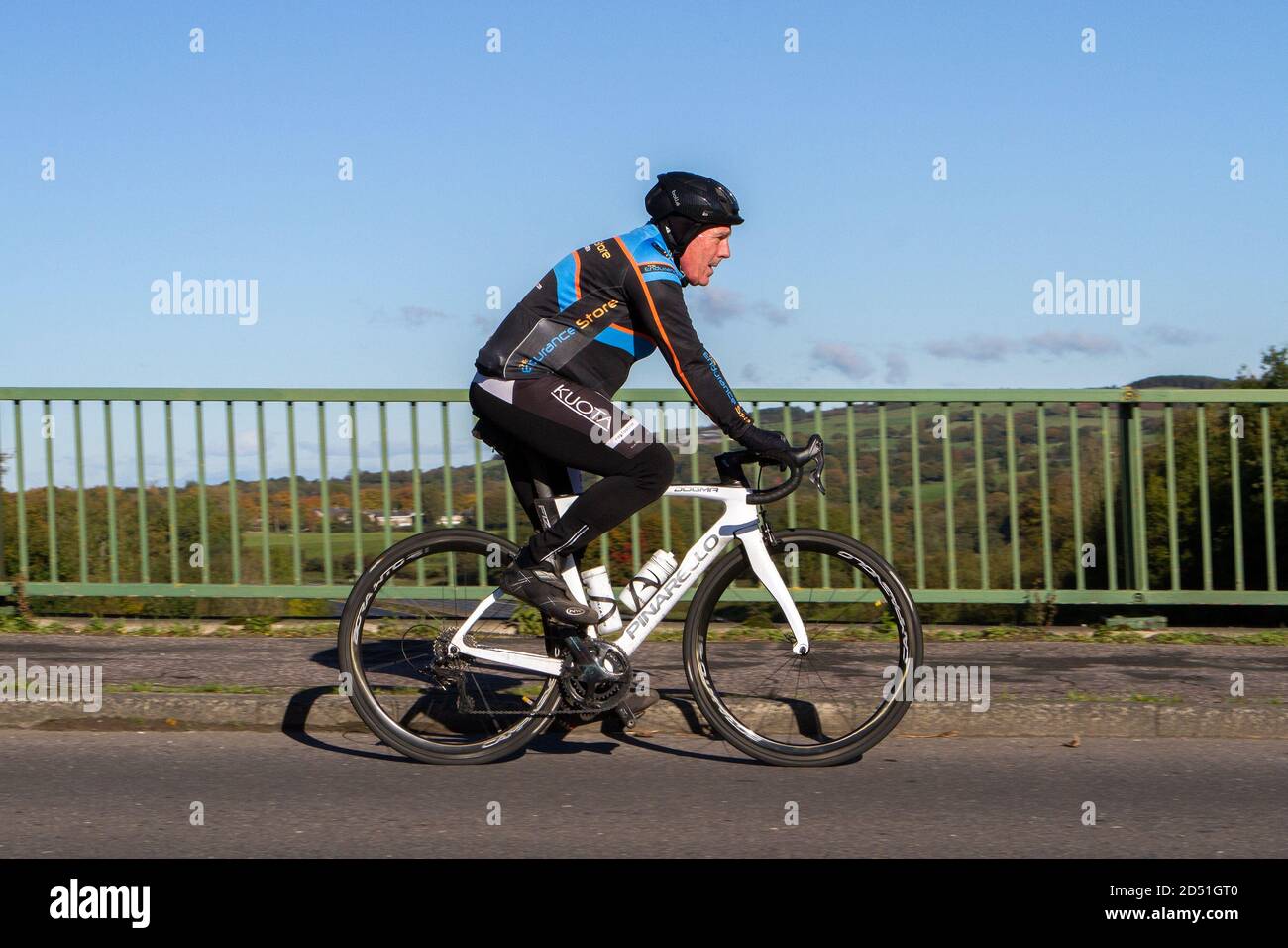 Male cyclist riding a Pinarello Dogma carbon fibre sports road bike bicycle on countryside route crossing motorway bridge in rural Lancashire, UK Stock Photo
