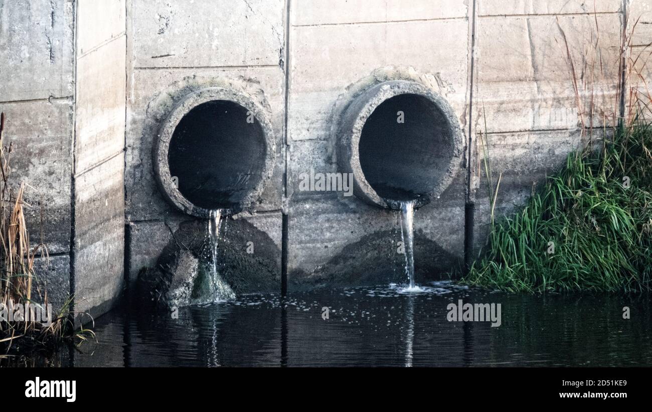 Gutter. Water runoff from a street spillway (water disposal, storm drain), two pipes and slow-flowing water (direct runoff) after rain Stock Photo