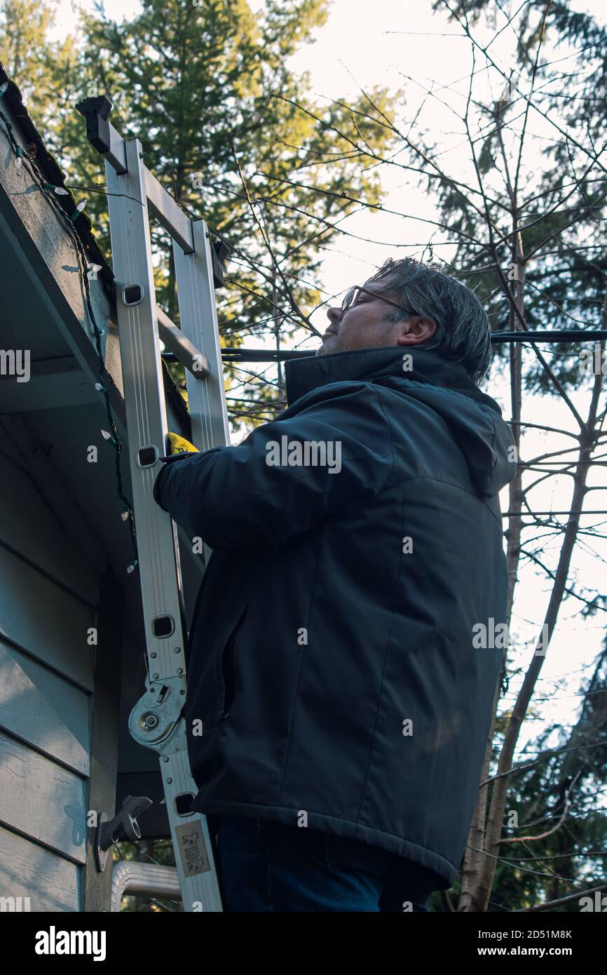 father and adult son hanging Christmas lights on the gutter with a