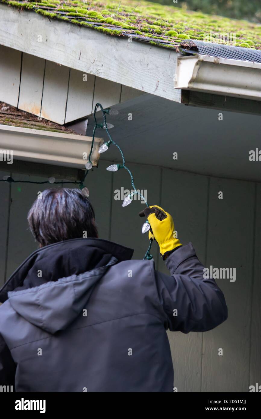 father and adult son hanging Christmas lights on the gutter with a