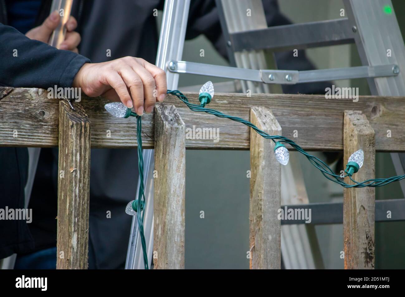 father and adult son hanging Christmas lights on the gutter with a