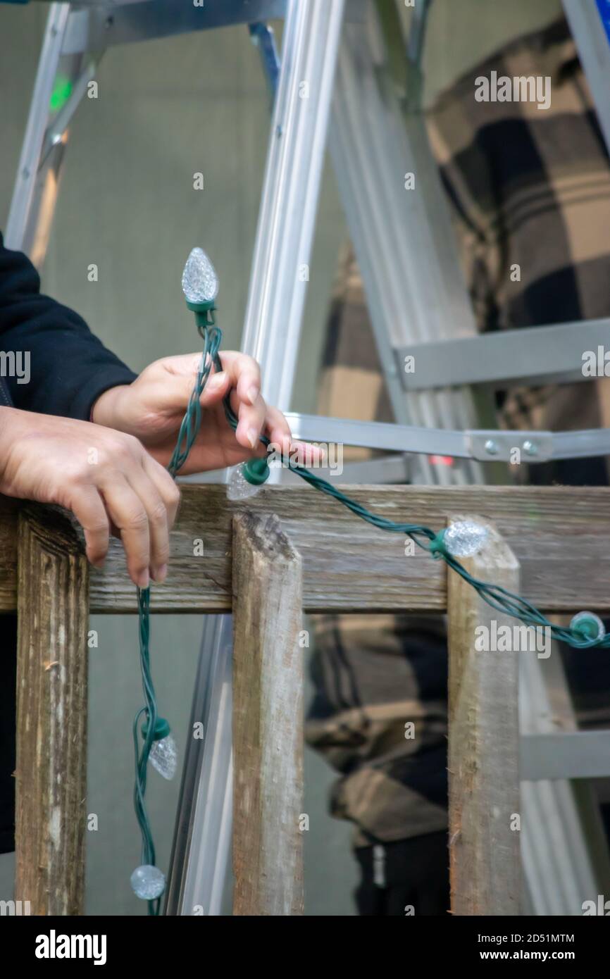 father and adult son hanging Christmas lights on the gutter with a