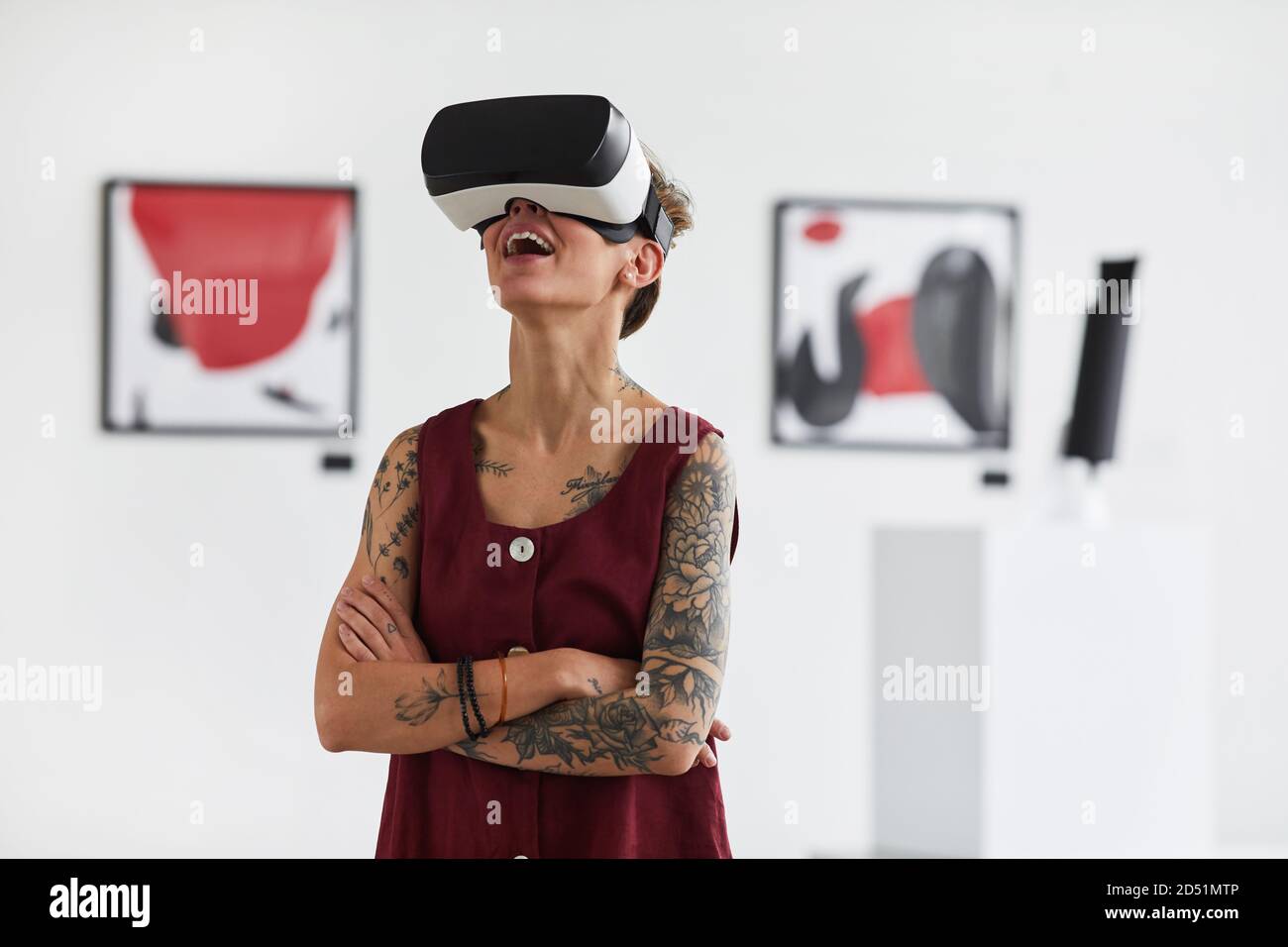 Waist up portrait of tattooed young woman wearing VR gear while enjoying immersive experience at modern art gallery exhibition, copy space Stock Photo