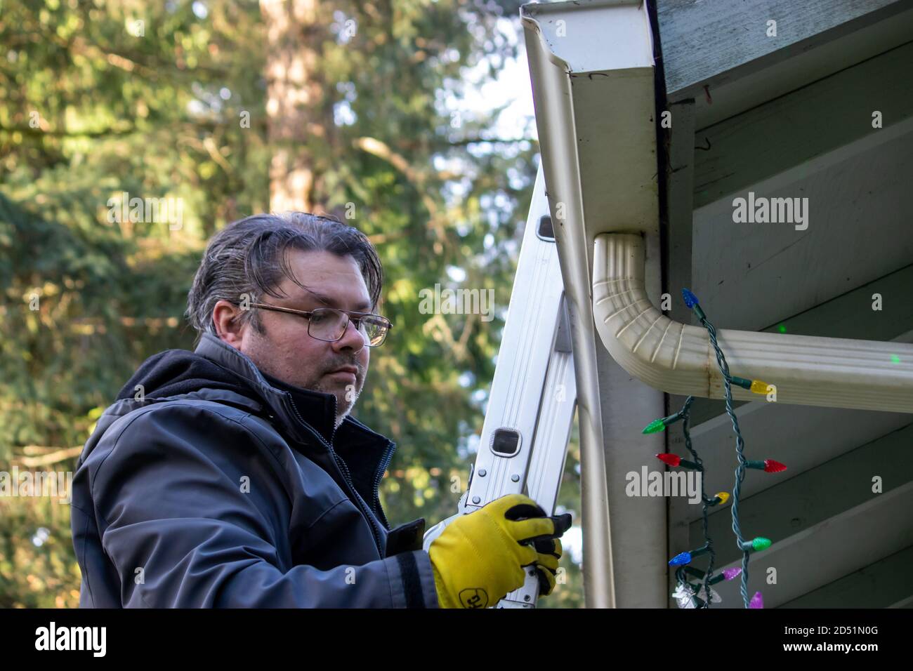 father and adult son hanging Christmas lights on the gutter with a