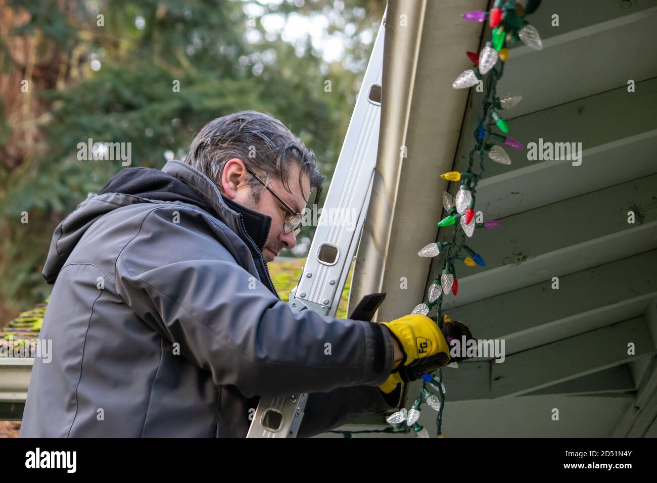 father and adult son hanging Christmas lights on the gutter with a