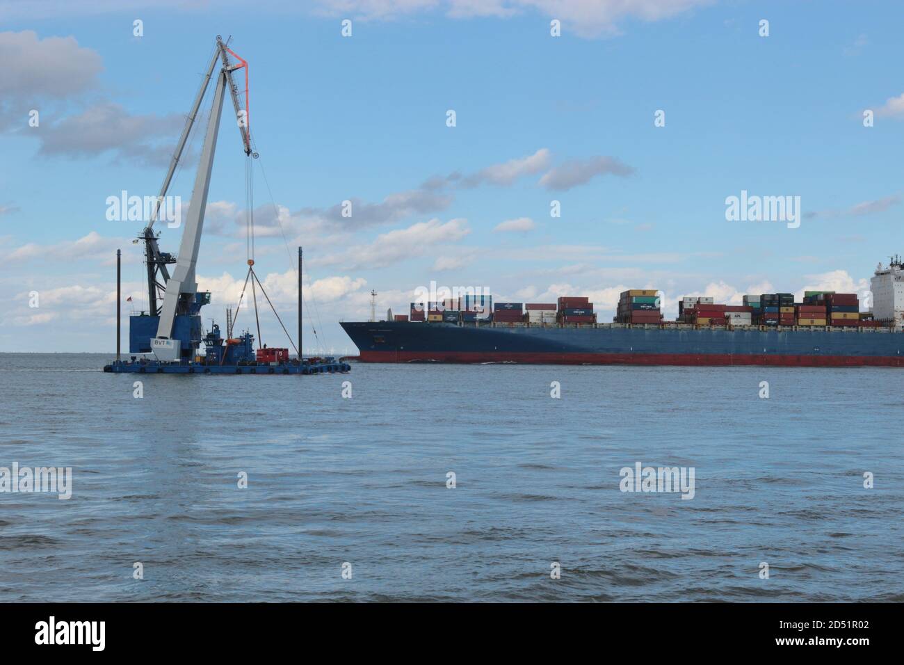 A working ship and a container ship passing the rivermouth of the Elbe, at high tide. Here the Elbe river flows into the North Sea. Cuxhaven, Germany. Stock Photo