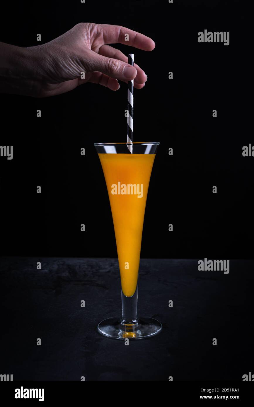 Woman hand putting paper straw in tall glass with pumpkin non-alcoholic mocktail standing on black textured stone table surface. Halloween no plastic Stock Photo