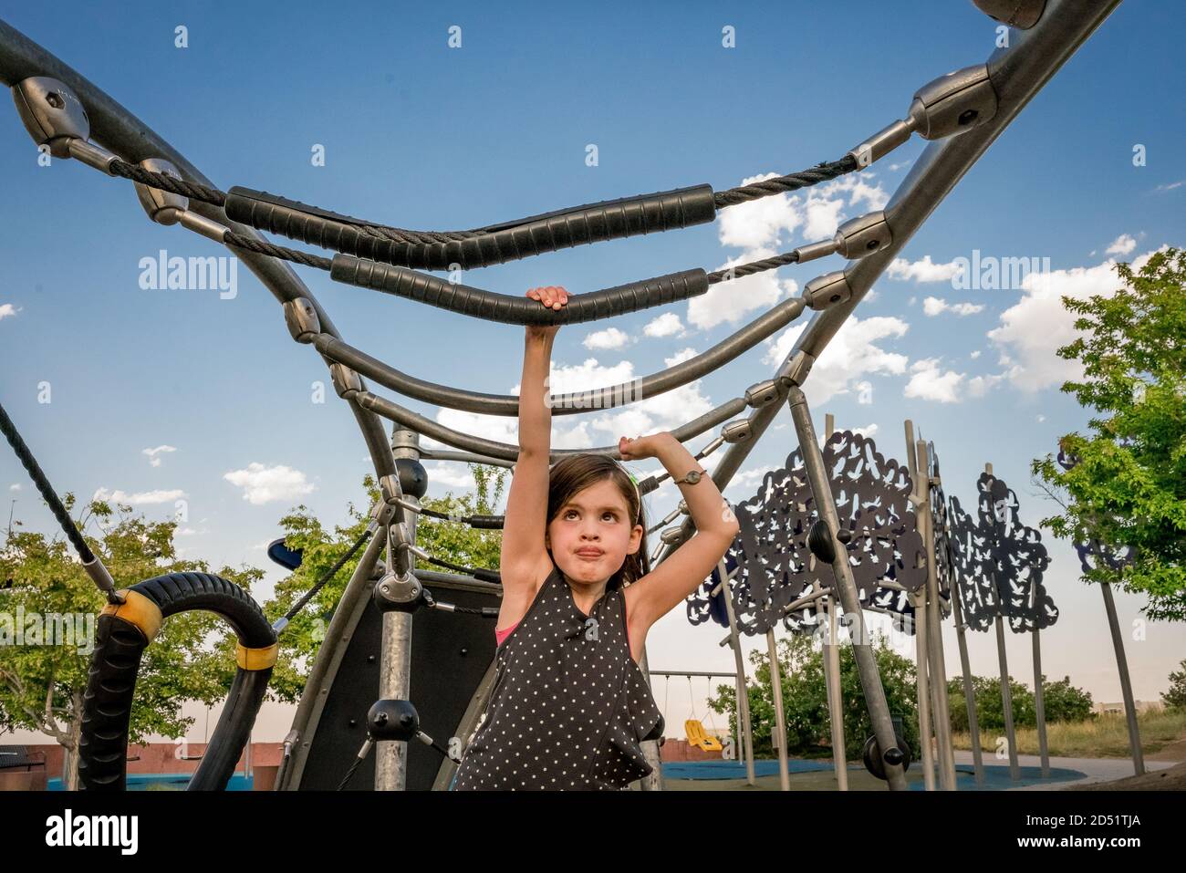 young girl concentrates as she plays on the monkey bars at playground Stock Photo