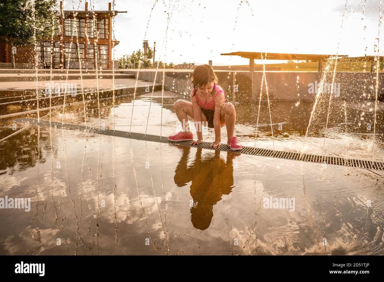 young girl in bathing suit squats over splash pad of squirting water Stock Photo