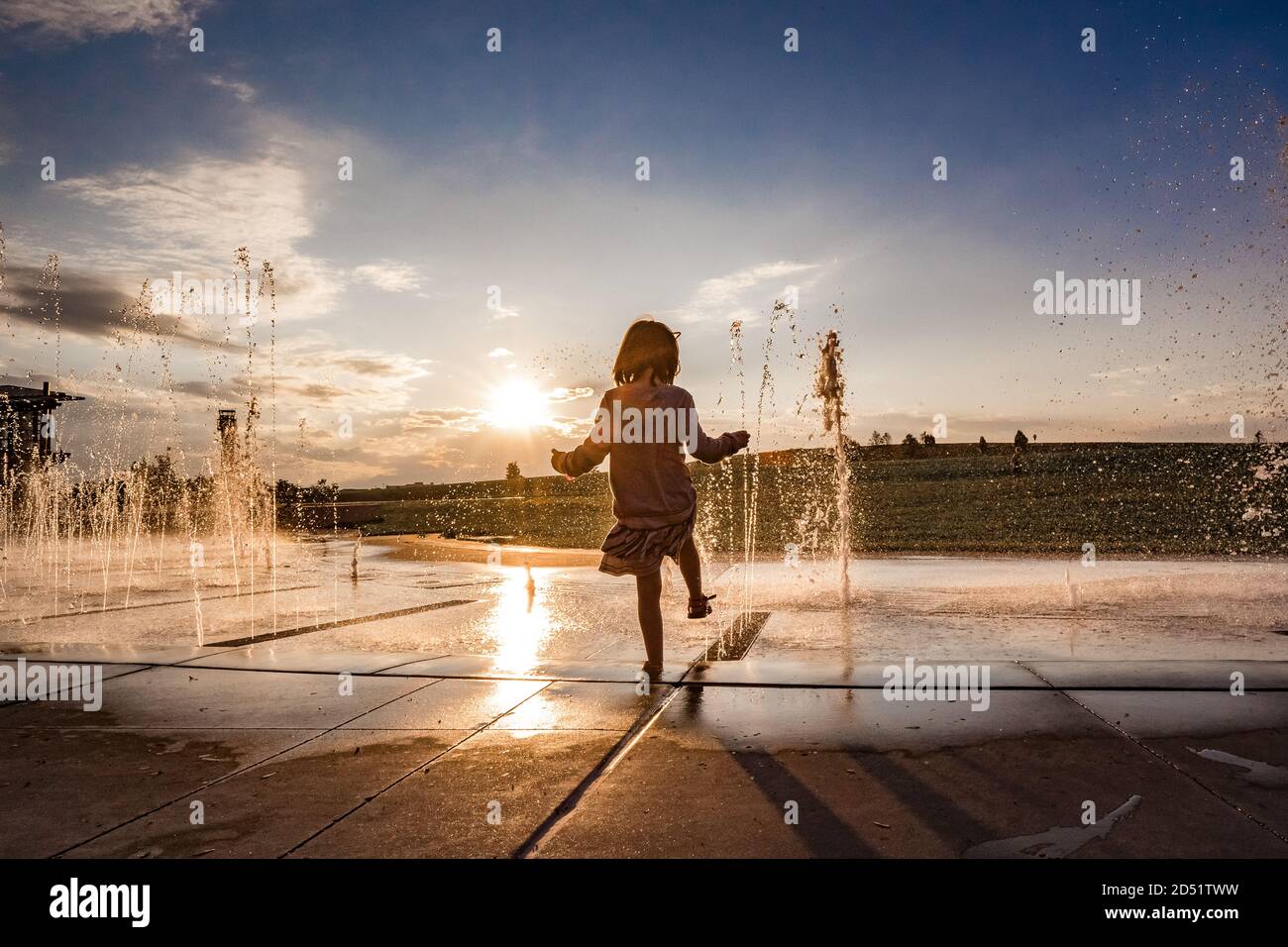 young girl hold her foot in the water at a splash pad at sunset Stock Photo