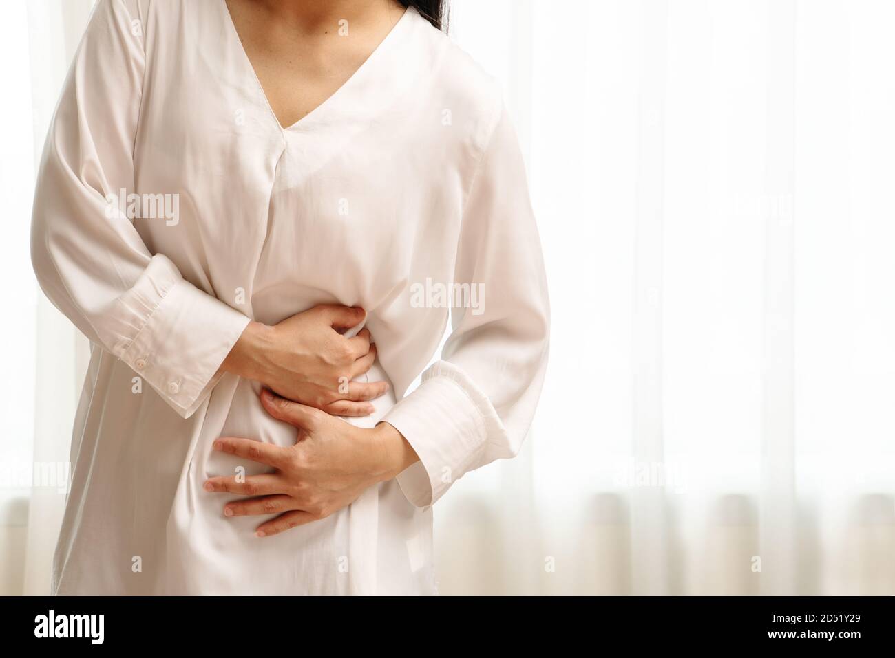 Young woman suffering from abdominal pain feeling stomachache, symptom of pms on white background Stock Photo