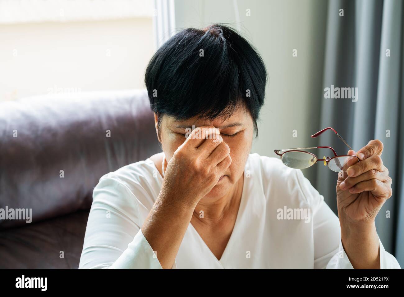 Tired old woman removing eyeglasses, massaging eyes after reading paper