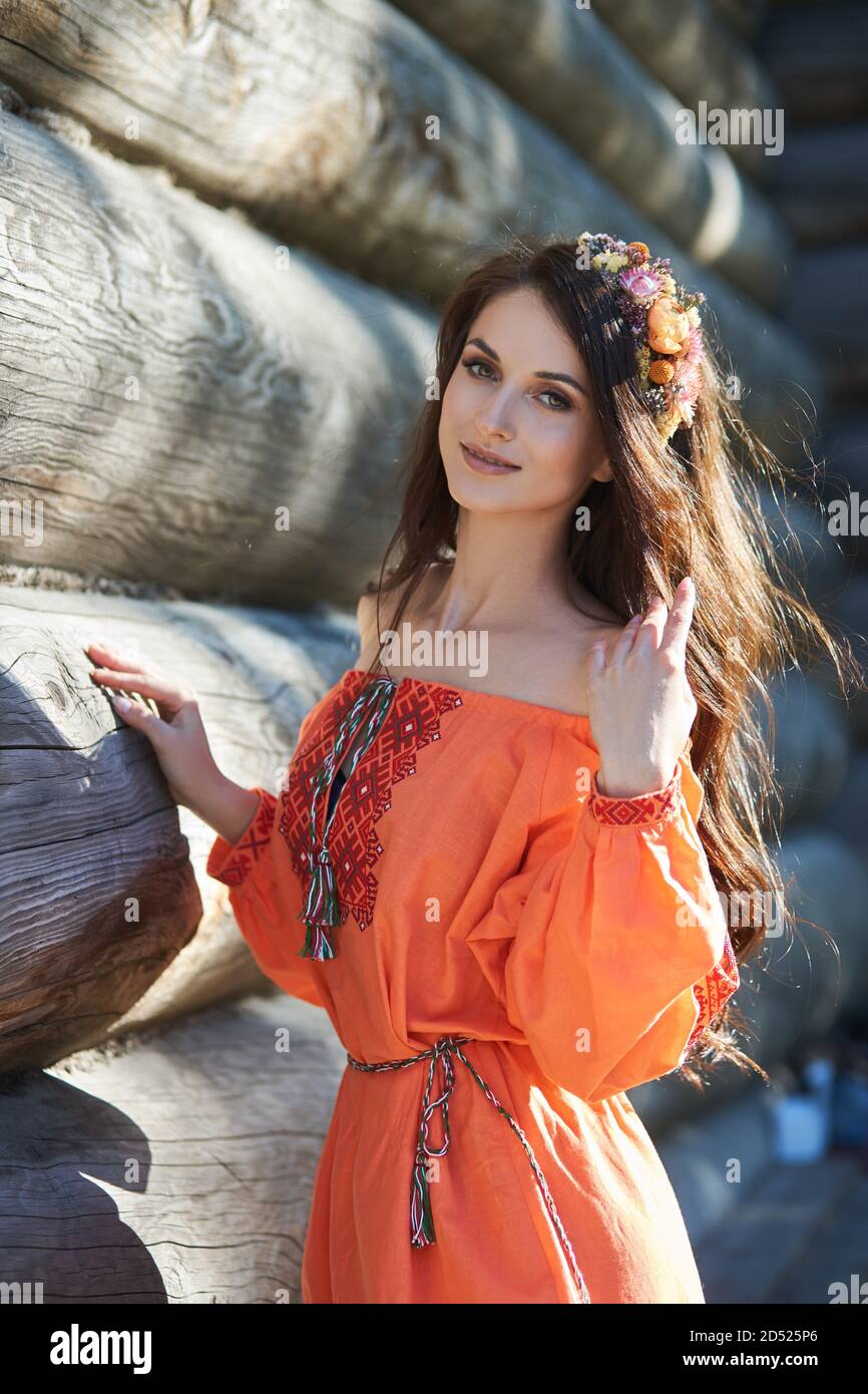 Beautiful Slavic woman in an orange ethnic dress and a wreath of flowers on her head. Beautiful natural makeup. Portrait of a Russian girl Stock Photo