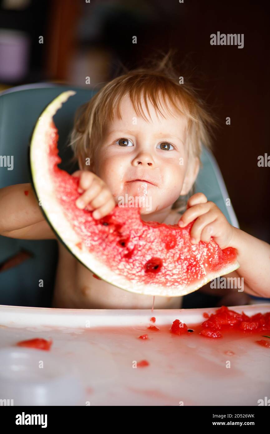 Happy toddler boy eating watermelon in his highchair Stock Photo Alamy