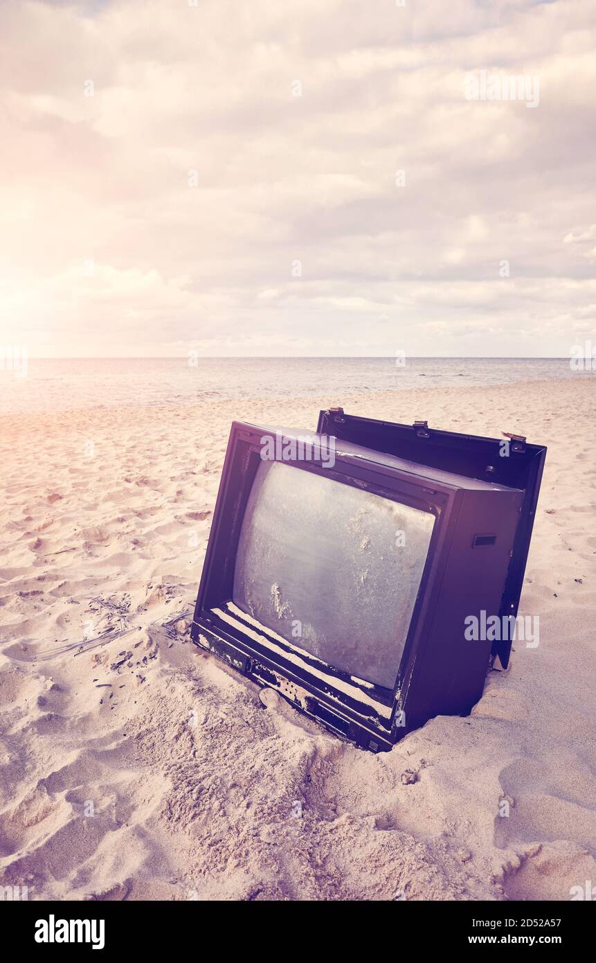 Old broken TV set on a beach at sunset, color toning applied, selective focus. Stock Photo