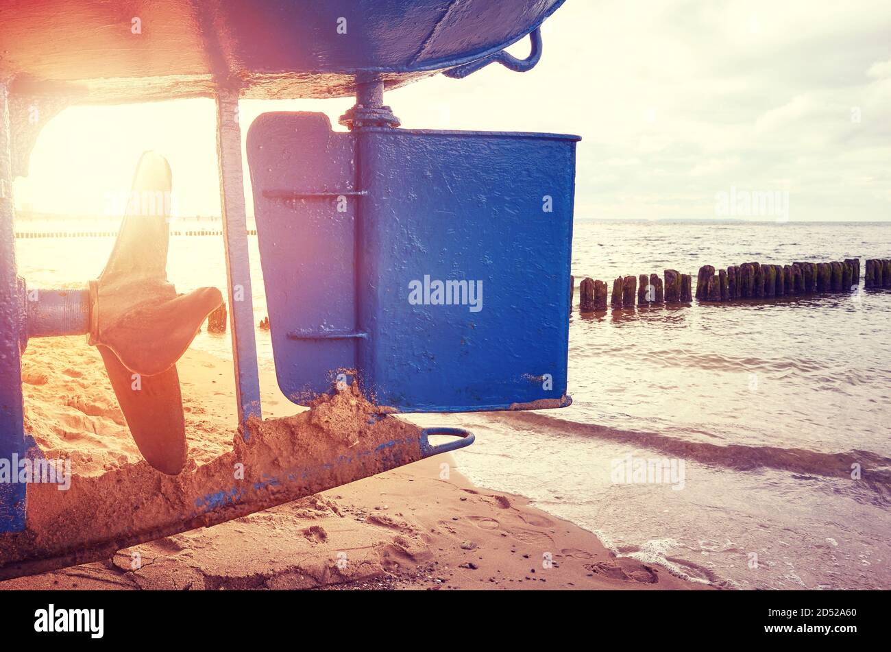Fishing boat rudder and propeller on a beach at sunset, color toning applied. Stock Photo