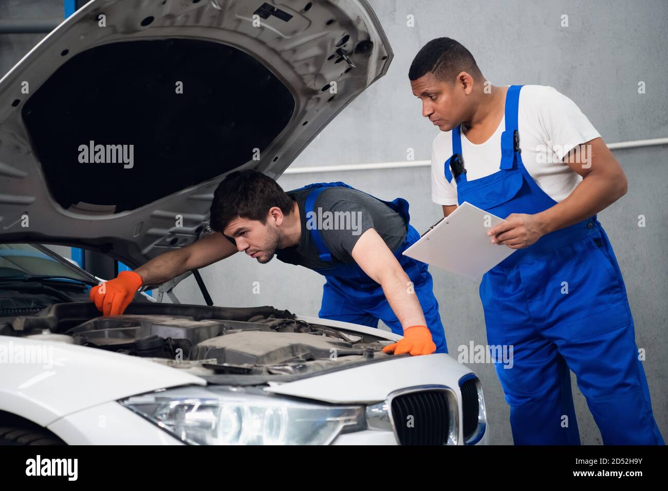 A in blue uniform repairing a broken engine of a car. His colleague ...