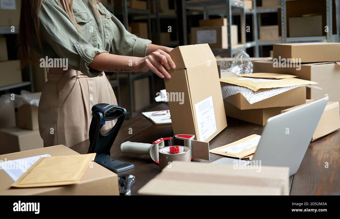 Female small business owner packing ecommerce order package in box at table. Stock Photo