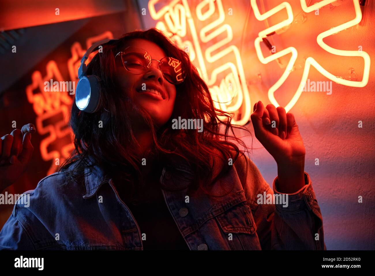 Happy African American lady wearing headphones listening music in neon light. Stock Photo