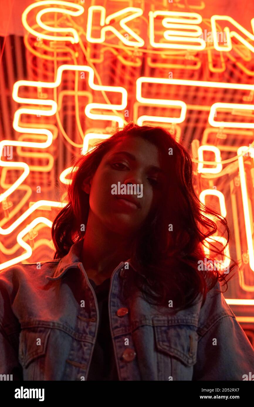 Hipster cool African gen z lady looking at camera under red neon night light. Stock Photo
