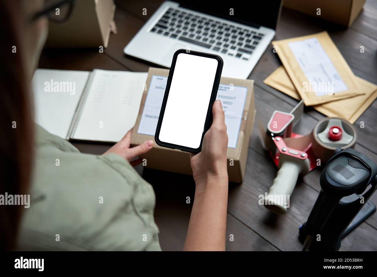 Female warehouse worker holding parcel box using mobile app on smartphone. Stock Photo