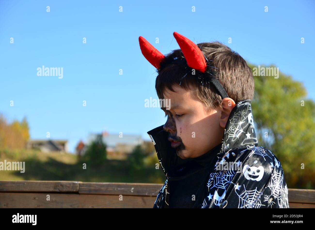 funny baby in devil halloween costume with horns and trident on a dark wooden background boy with black makeup for halloween, zombie Stock Photo