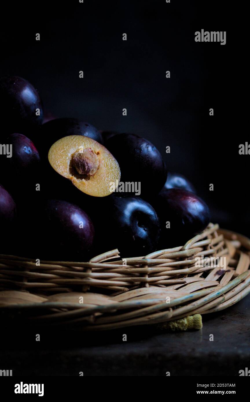 Vertical image of a pile of black plums, among which one half of them stands out on a dark background in the style of dark food and with copy space. Stock Photo