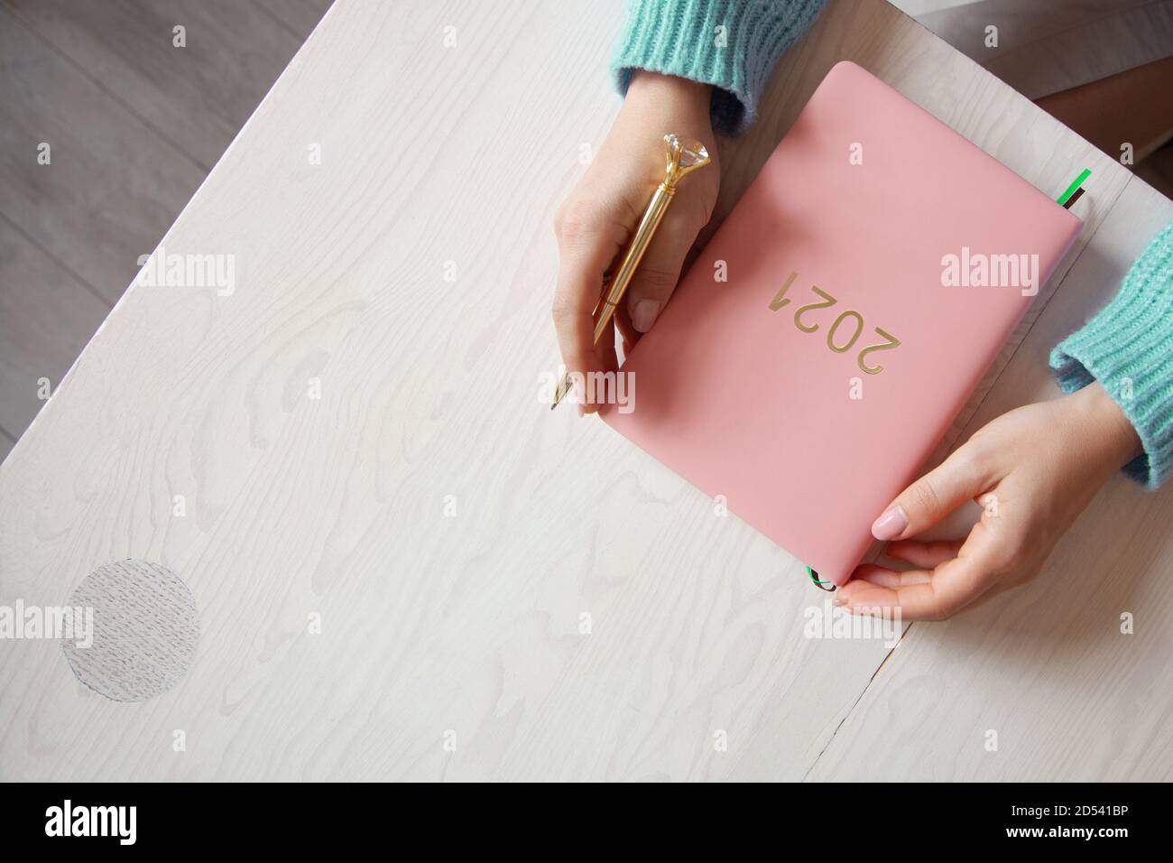 Woman sitting in knitted warm sweater with coral coloured 2021 diary on table Stock Photo