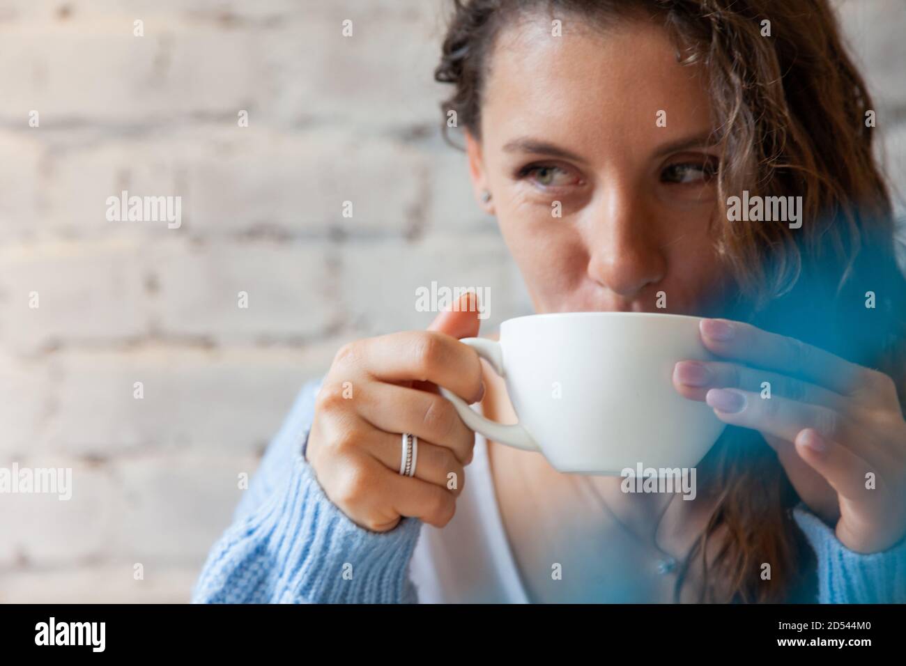 Happy young woman in knitted warm sweater holding with hands a cup of ...