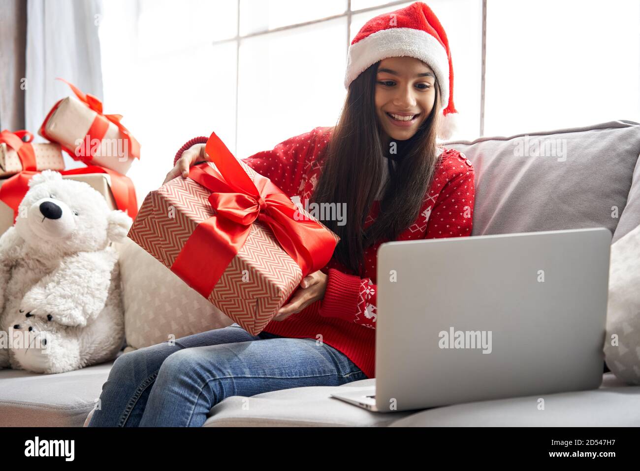 Happy indian girl wear santa hat holding gift video calling family on Christmas. Stock Photo