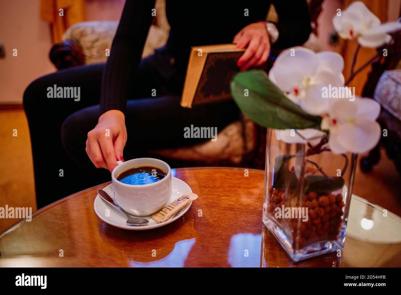 Selective focus shot of a woman drinking coffee while reading a book Stock Photo