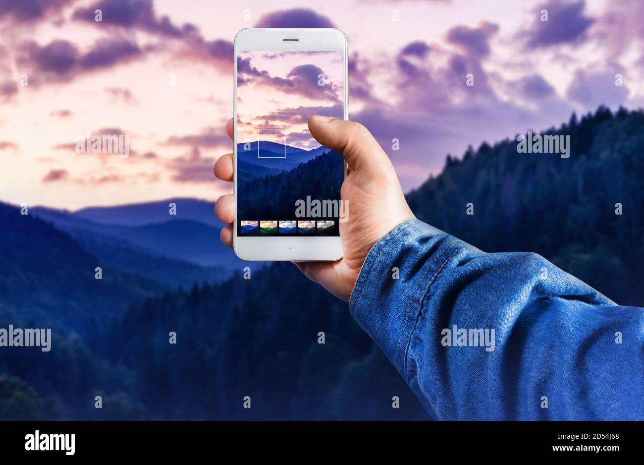 First person view photo of a male hand in jeans shirt holding smartphone and taking photo and using application in forest mountains. Stock Photo