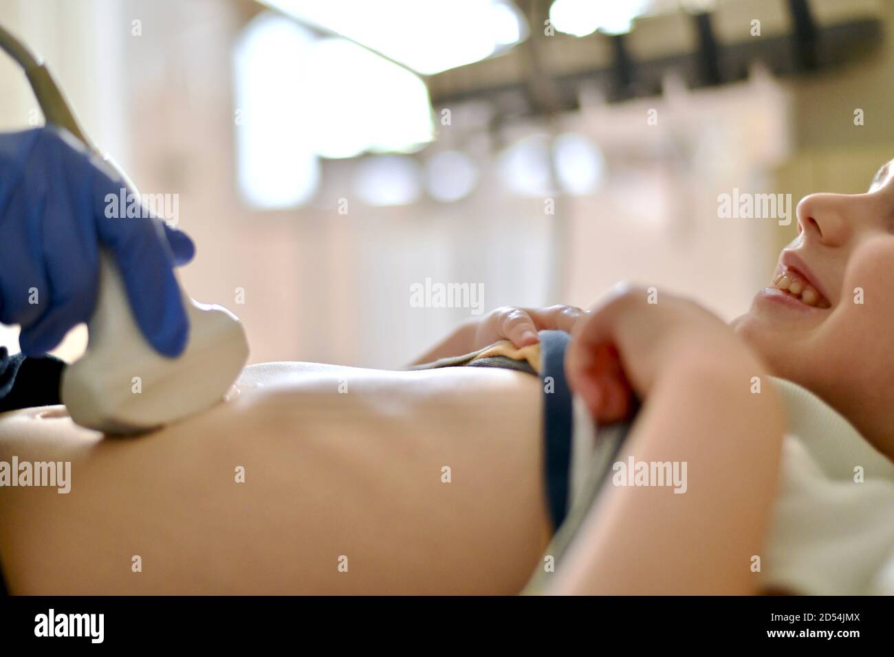 A smiling kid on a medical ultrasound examination. Examination of hand sensor in protective gloves. Stock Photo