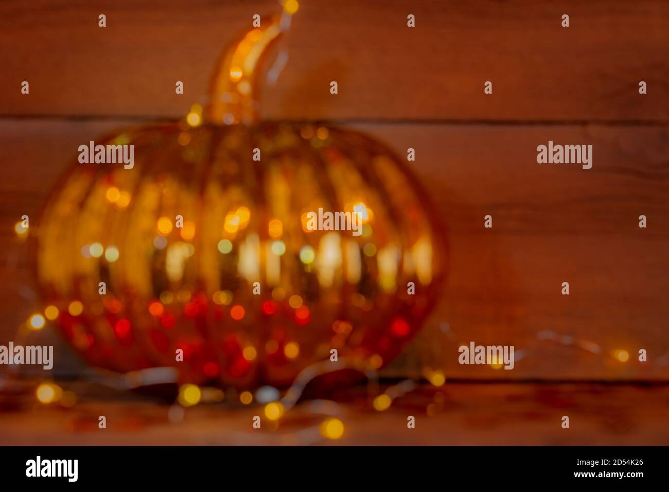 A single glass pumpkin is in soft focus and abstracted and is wrapped in lights on a wooden shelf. Stock Photo