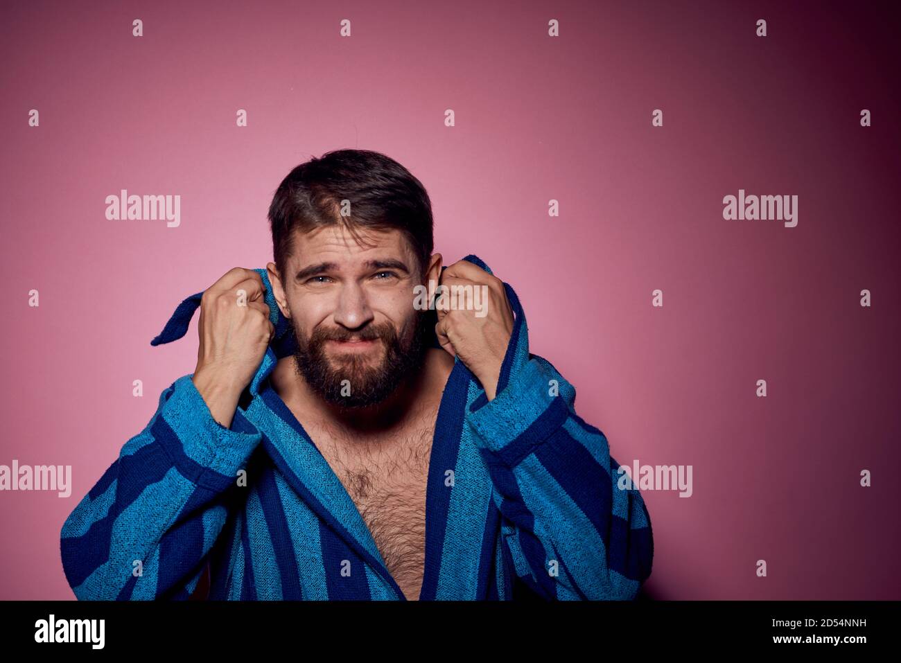 Bearded man in a blue striped robe on a pink background with hands ...